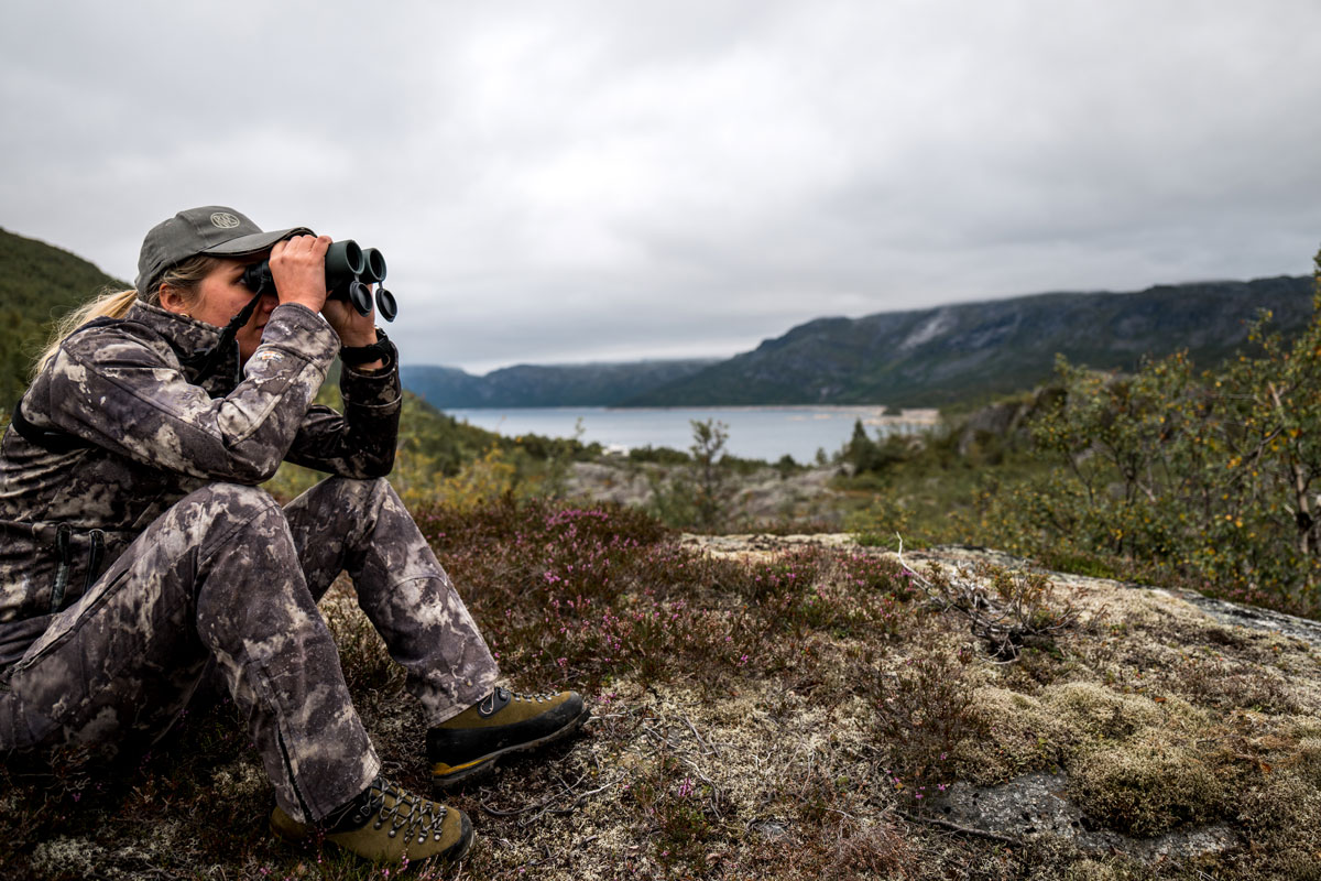 Jagen am Limit – auf Rentiere in Norwegen Frau in Tarnklamotten schaut mit Fernglas in die Ferne