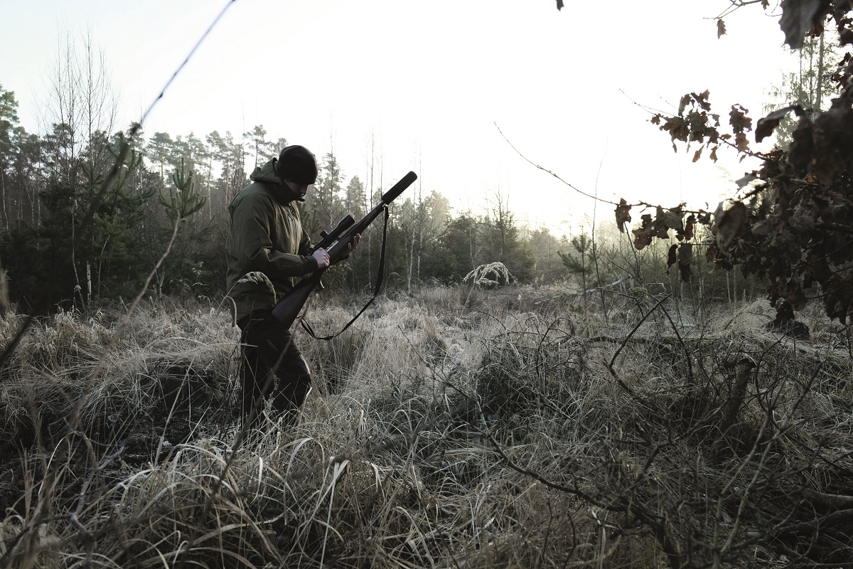 Jäger steht mit Gewehr und Schalldämpfer im Wald